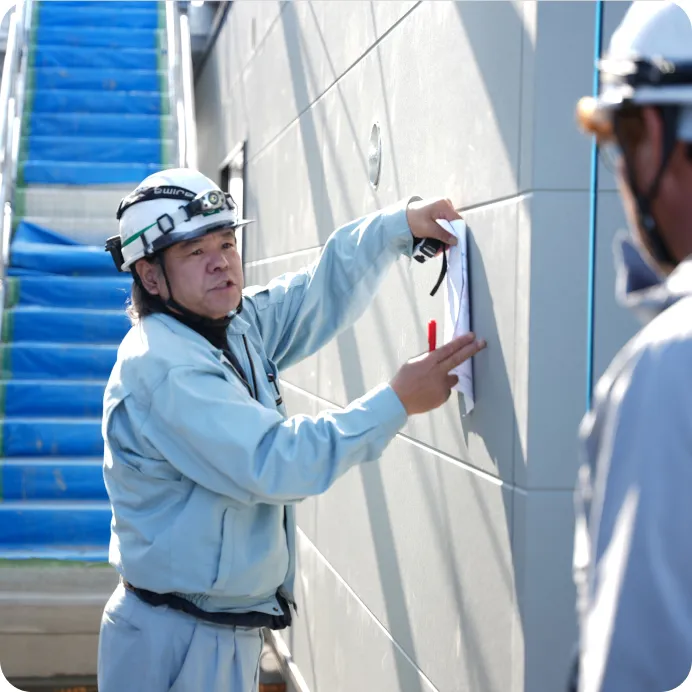 現場の壁に図面を当て、赤いペンで指し示しながら打ち合わせをするヘルメット姿の作業員