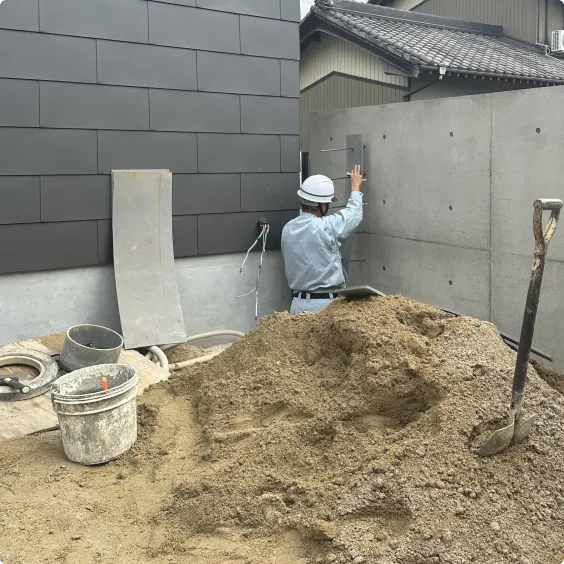 コンクリート壁の施工作業を行う作業員と手前の砂山