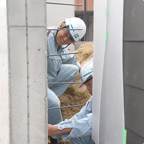 現場で笑顔を見せながら協力して作業を行う2人の作業員