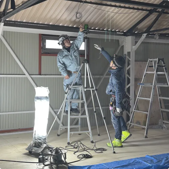 室内現場で測量機器(レーザー墨出し器)を使用して作業する2人の作業員