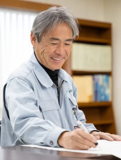 笑顔で書類にペンを走らせるT・Iさんのクローズアップ。